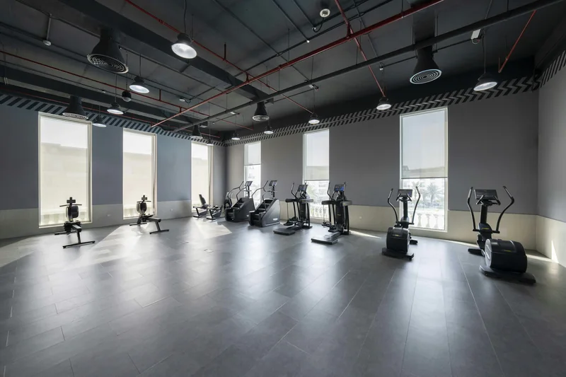 An empty gym with cardio equipment beside large windows.
