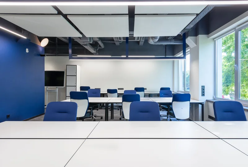 An empty modern office with white desks, blue chairs and large windows.